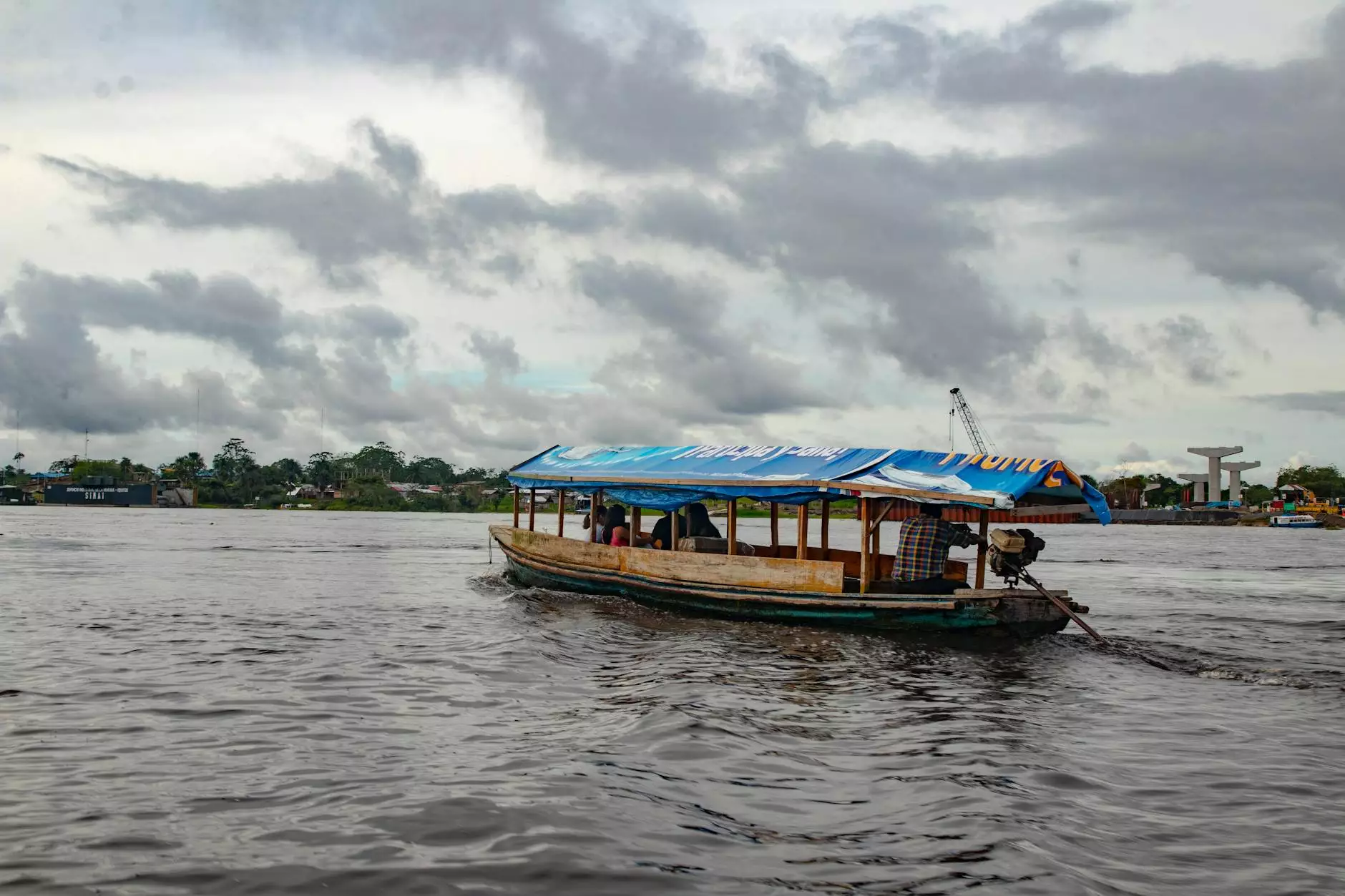 A covered wooden boat crossing a broad river beneath a cloudy sky